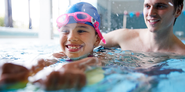 Bilden visar ett barn som försöker lära sig simma med hjälp av en vuxen i en pool