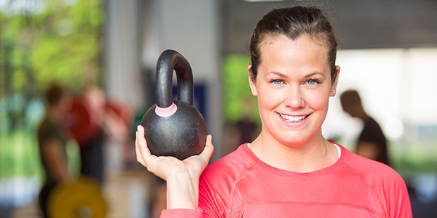 Bilden visar en tjej på gymmet som lyfter upp en kettlebell med ena armen
