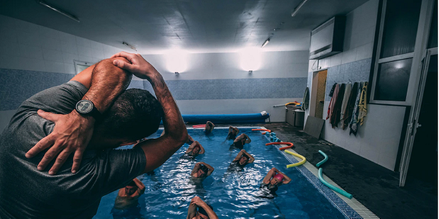 Bilden visar en pool där några personer står på varsin träningsmatta i vattnet framför en instruktör